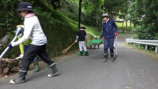 市村自然塾関東の塾生が、塾舎と農場との間の道路をホウキなどで清掃している